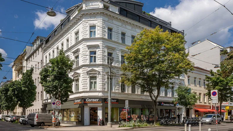 Historisches Eckgebäude mit moderner Dachaufstockung und Geschäften im Erdgeschoss an einer belebten Straße.