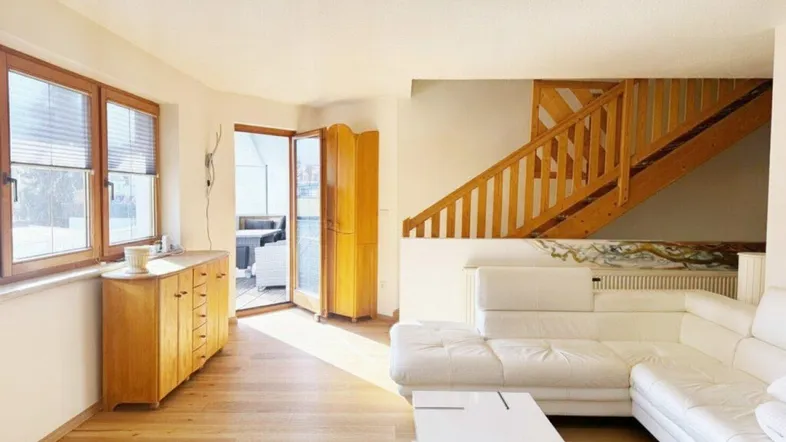 Helles Wohnzimmer mit Holzboden, weißem Sofa und Zugang zu einem Außenbereich.