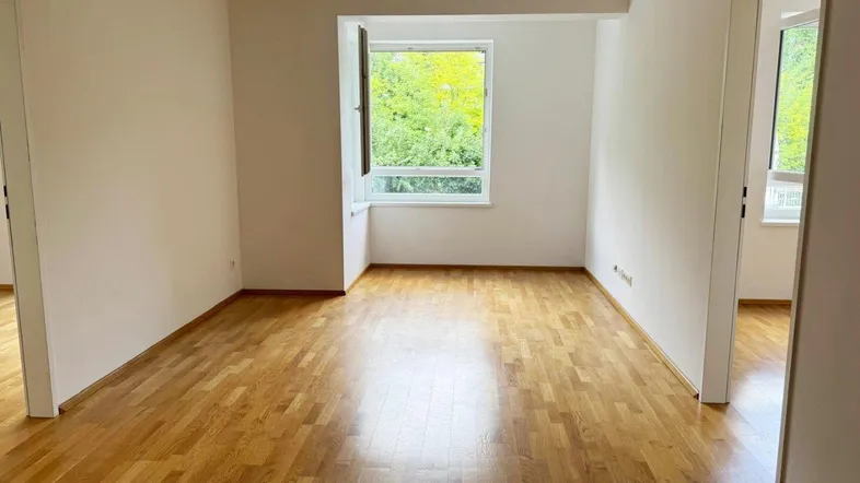 Helles, leeres Zimmer mit Parkettboden und Blick ins Grüne, bereit zur individuellen Gestaltung.