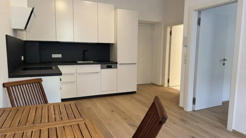 Moderne Einbauküche mit weißen Schränken, dunkler Arbeitsplatte und Holzboden, offen zum Essbereich.