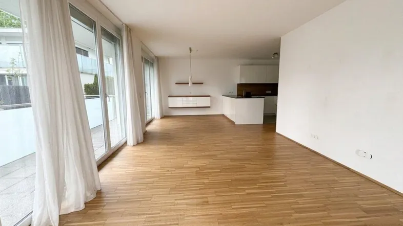 Helles Wohnzimmer mit Parkettboden, großen Fensterfronten und offenem Zugang zur Küche.