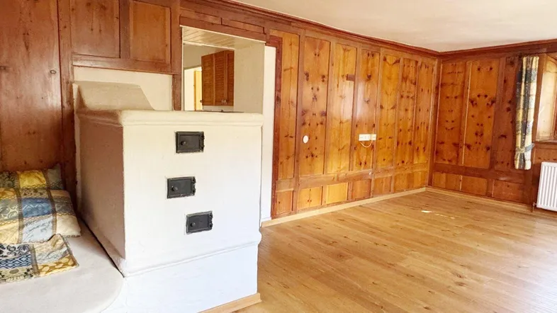 Gemütliches Zimmer mit Holztäfelung, traditionellem Kachelofen und hellem Holzfußboden.