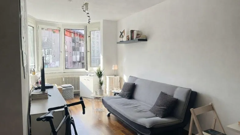 Helles Wohnzimmer mit Erkerfenstern, Holzboden und einem bequemen Sofa.