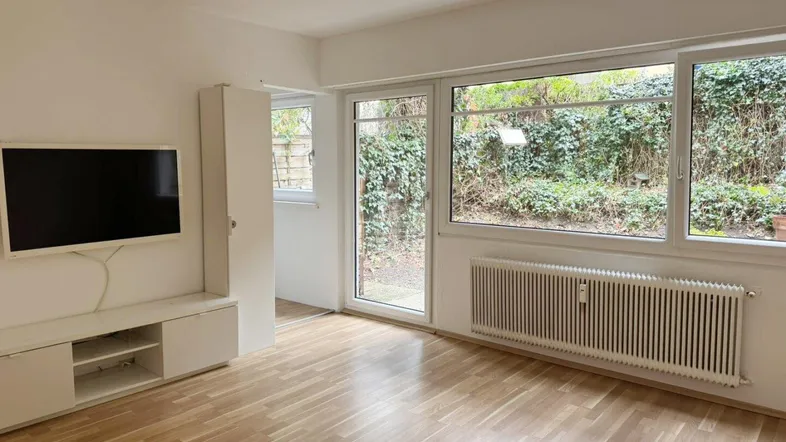 Helles Wohnzimmer mit Holzboden, großen Fenstern und direktem Zugang zum Gartenbereich.