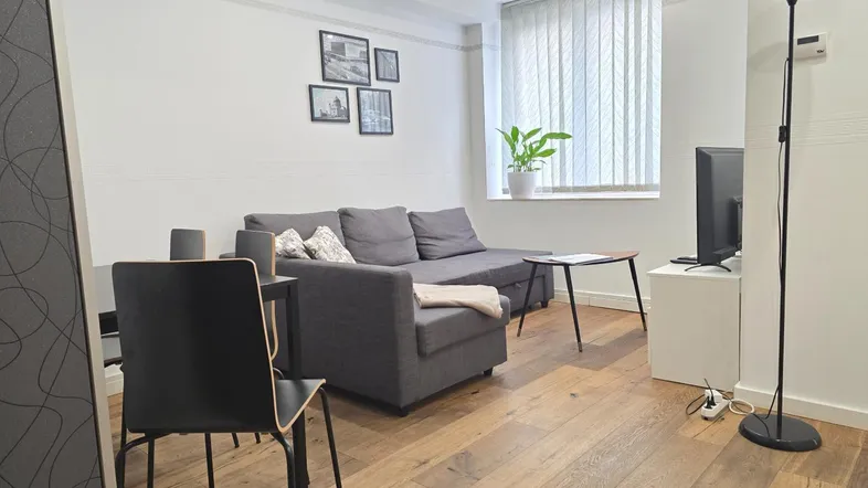 Helles Wohnzimmer mit modernem Sofa, Holzboden und großem Fenster mit Jalousien.