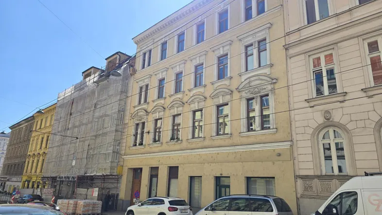 Historisches Gebäude mit gelber Fassade und vielen Fenstern an einer belebten Stadtstraße.