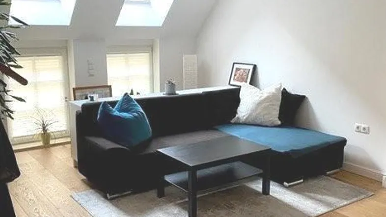 Helles Wohnzimmer mit Holzboden, gemütlichem Sofa und Dachfenstern unter einer schrägen Decke.