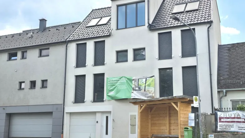 Modernes Mehrfamilienhaus mit Schrägdach, Dachgaube und integrierten Garagen an einer Straße gelegen.