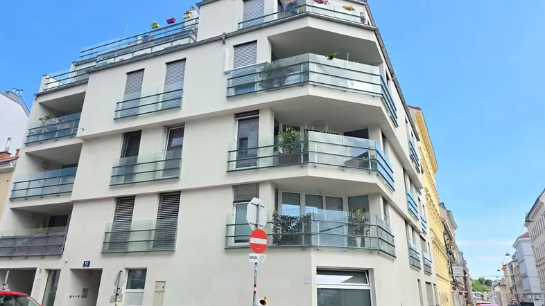 Modernes Mehrfamilienhaus mit mehreren Balkonen und Glasgeländern in städtischer Umgebung.