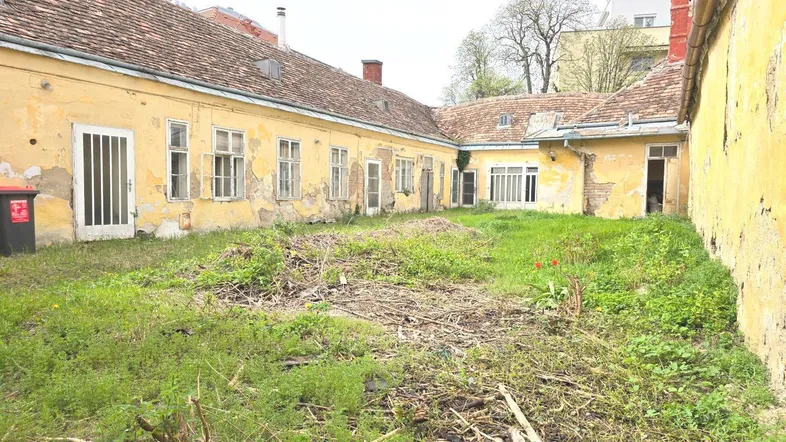 Ungepflegter Innenhof mit Rasenfläche und alten Gebäudefassaden, die auf eine Renovierung warten.