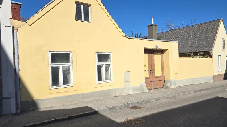Gelbes Gebäude mit Giebeldach und Holztür von der Straße aus gesehen unter blauem Himmel.