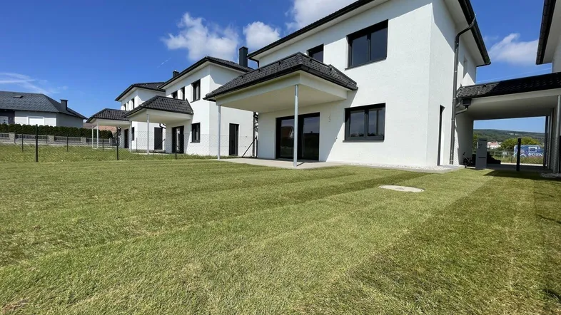 Moderne Reihenhäuser mit frisch angelegtem Rasen und sonnigem Gartenbereich.