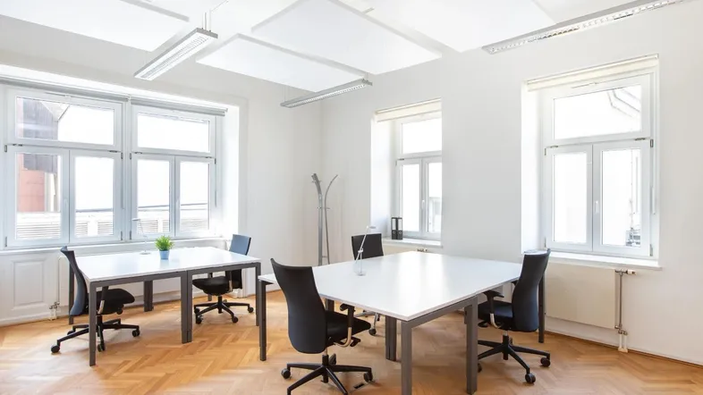 Helles Büro mit mehreren Arbeitsplätzen, großen Fenstern und Fischgrätparkettboden, ideal für produktives Arbeiten.
