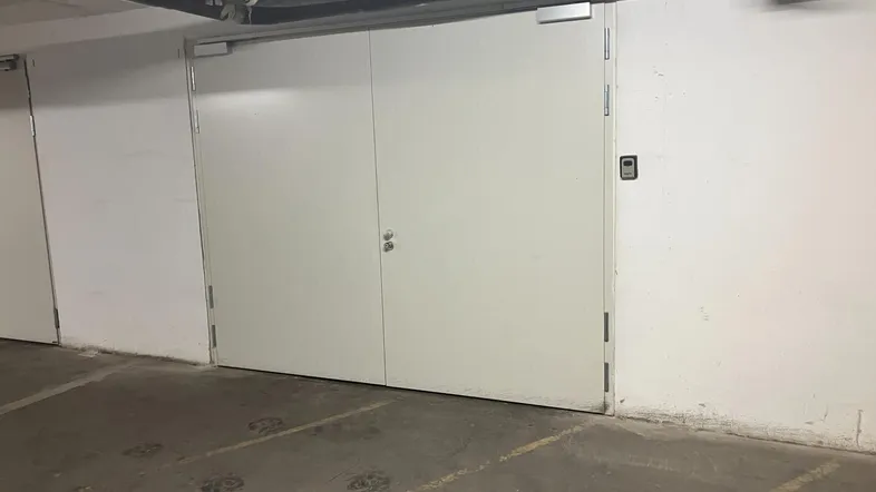 Tiefgaragenstellplatz mit robusten weißen Türen und sichtbaren Versorgungsleitungen an der Decke.