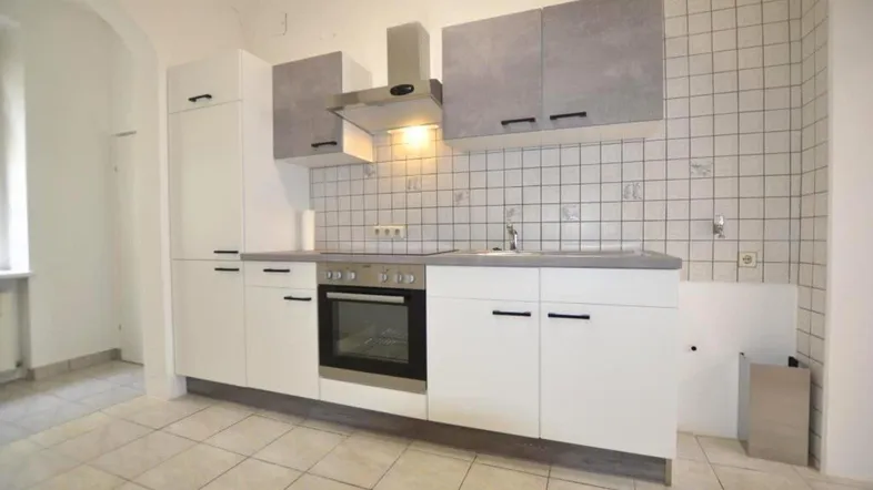 Helle Küche mit weißen und grauen Schränken, Fliesenrückwand und integriertem Backofen.