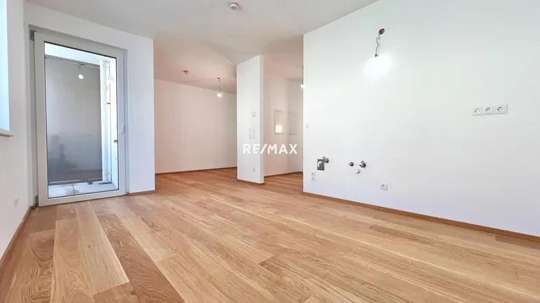 Heller, unmöblierter Raum mit Holzboden und Balkonzugang, vorbereitet für eine moderne Küche.