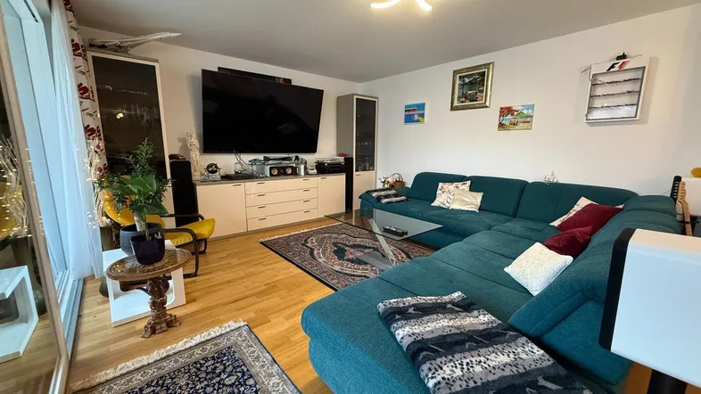 Geräumiges Wohnzimmer mit bequemer Eckcouch, Holzboden und Zugang zu einem Balkon.