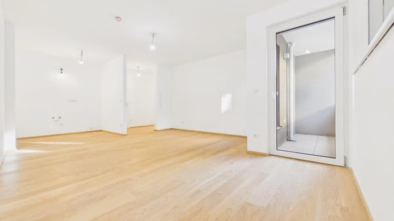 Heller, leerer Raum mit Holzparkettboden und Zugang zu einem Balkon oder einer Terrasse.