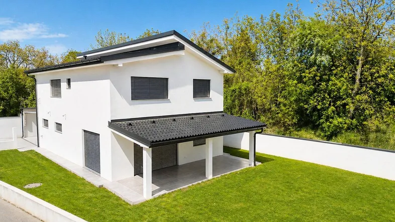 Modernes Einfamilienhaus mit weißer Fassade, schwarzem Dach und gepflegtem Rasen in sonniger Lage.