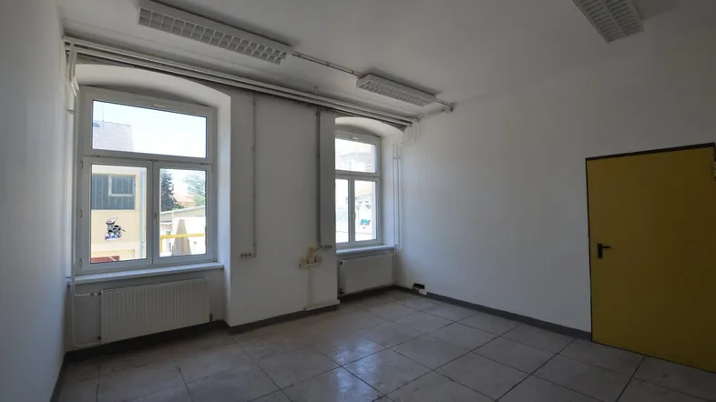 Leerer Raum mit weißen Wänden, zwei Fenstern, gelber Tür und Fliesenboden.