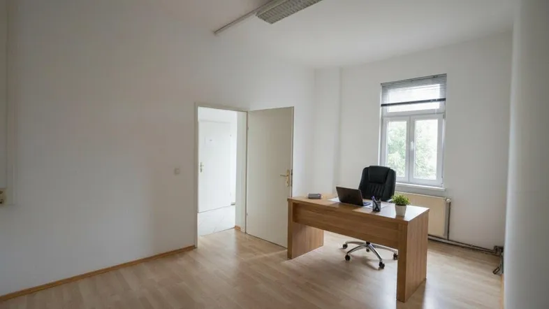 Helles Büro mit Laminatboden, einem Schreibtisch und einem Fenster, das viel Tageslicht hereinlässt.