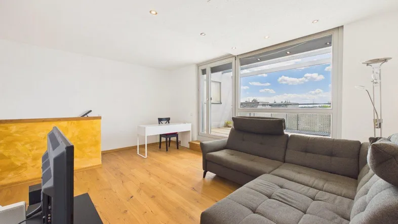 Helles Wohnzimmer mit Holzboden, großem Sofa und Zugang zur Terrasse mit Weitblick.