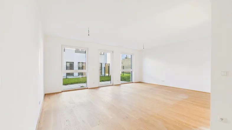 Helles Wohnzimmer mit Holzboden und großen Fenstern, die Zugang zu einer kleinen Grünfläche bieten.