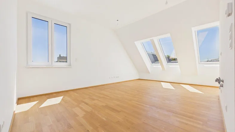 Helles Dachgeschosszimmer mit Holzboden und mehreren Fenstern, inklusive Dachfenstern.