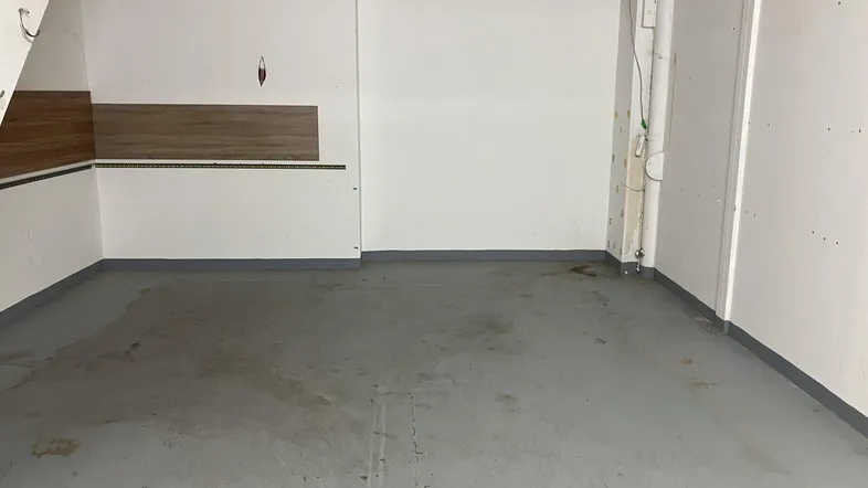Geräumiger Lagerraum mit grauem Betonboden und weißen Wänden, ideal für Abstellzwecke im Untergeschoss.