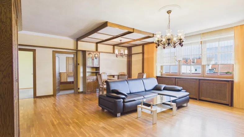 Geräumiger Wohn- und Essbereich mit Parkettboden, dunklem Sofa und traditioneller Holzdecke.
