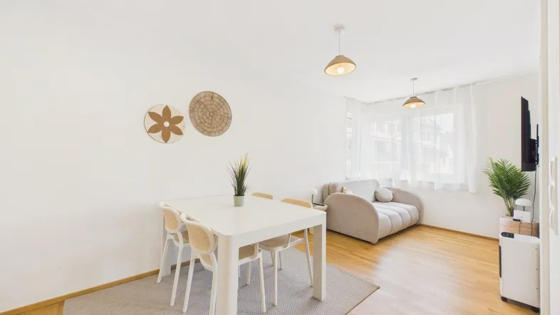 Heller Wohn- und Essbereich mit Holzboden, modernem Esstisch und beigem Sofa.