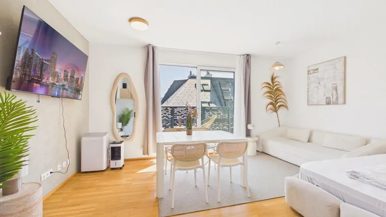 Helles, offenes Wohn- und Schlafzimmer mit Holzboden, Essbereich und Zugang zum Balkon.