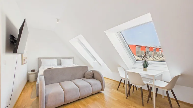 Helles Dachgeschosszimmer mit Bett, Sofa, Esstisch und großen Dachfenstern, die viel Licht hereinlassen.