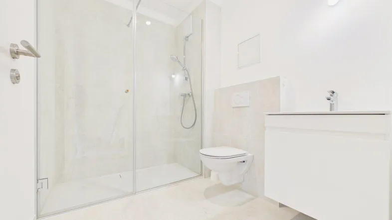 Modernes Badezimmer mit ebenerdiger Dusche, wandhängendem WC und hellem Fliesenboden.