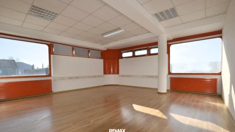Heller Büroraum mit großen Fenstern, Laminatboden und orangefarbenen Akzenten an den Wänden.