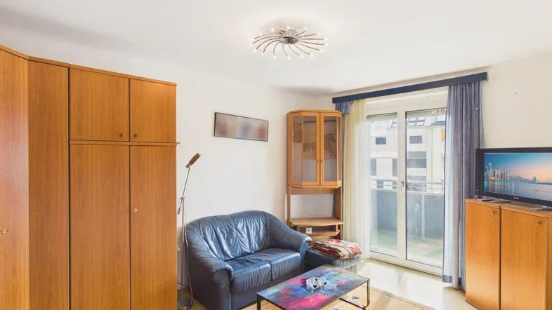 Helles Wohnzimmer mit blauer Couch, Holzschränken und Zugang zum Balkon.