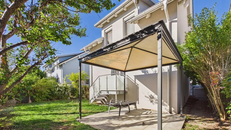 Gepflegter Gartenbereich mit Rasenfläche, Terrasse und einem schattenspendenden Pavillon hinter dem Haus.