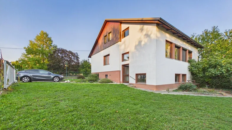 Weißes Einfamilienhaus mit Holzverkleidung im Giebelbereich und großem Rasen.