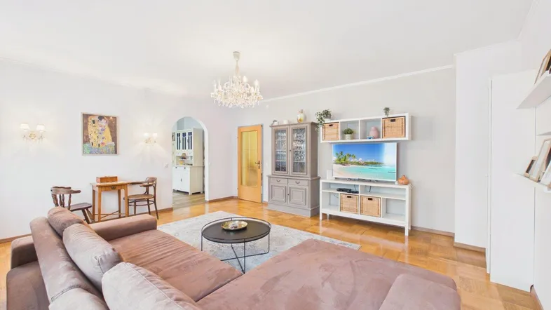 Gemütliches Wohnzimmer mit großem Sofa, Parkettboden und Kronleuchter, offen zum Essbereich.