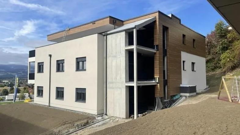 Neubau-Mehrfamilienhaus mit moderner Fassade, Holzverkleidung und Balkonen in Hanglage.
