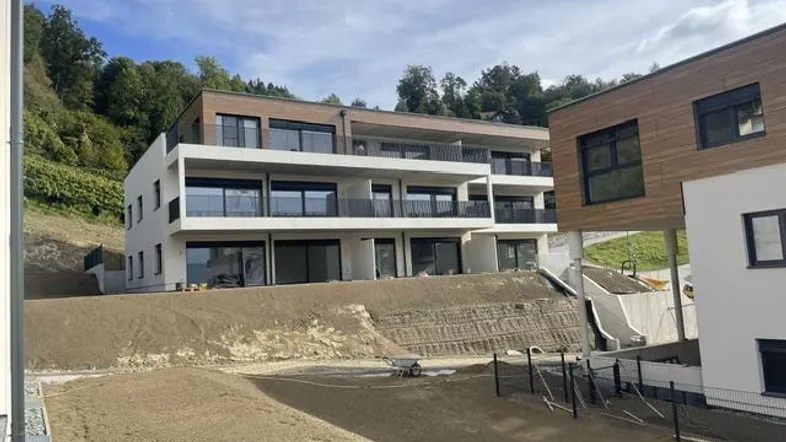 Modernes Mehrfamilienhaus im Bau mit großen Balkonen und Blick ins Grüne am Hang.