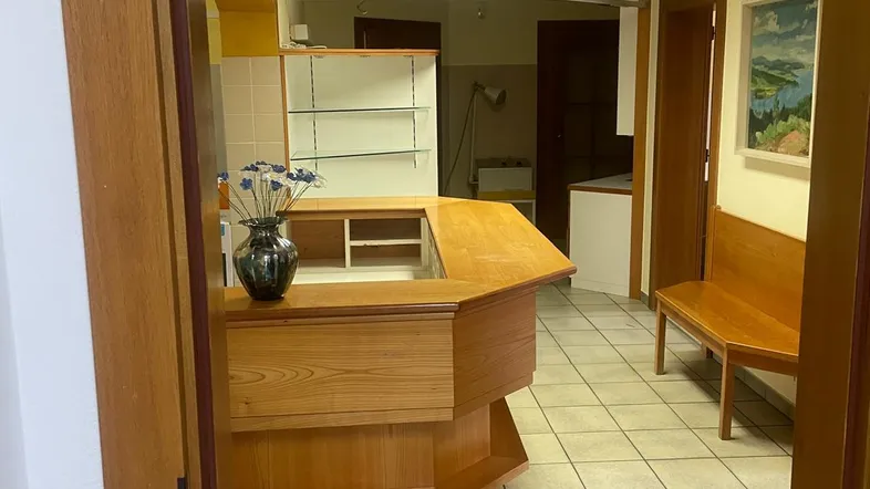 Blick in einen Empfangsbereich mit Holztheke, Regalen und gefliestem Boden.