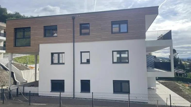 Moderne Architektur mit weißer Fassade und Holzverkleidung, ergänzt durch Balkone und eine grüne Umgebung.