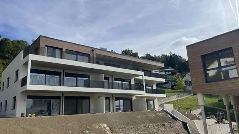 Modernes Mehrfamilienhaus im Bau mit Terrassen und Balkonen, umgeben von Natur.