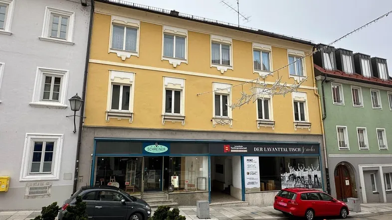 Gelbes Gebäude mit Geschäften im Erdgeschoss und Wohnungen darüber an einer Straße.