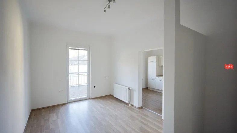 Helles Zimmer mit Holzboden, weiß gestrichenen Wänden und Zugang zu einem französischen Balkon.