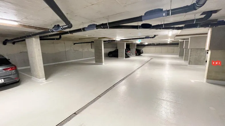 Geräumige Tiefgarage mit Betonstützen, freiliegenden Rohren und mehreren Parkplätzen für Bewohner.