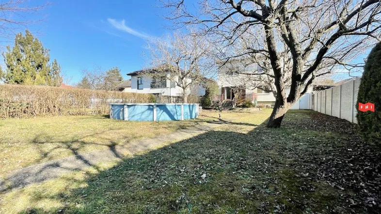 Großer Garten mit Rasenfläche, Bäumen und einem Aufstellpool unter blauem Himmel.