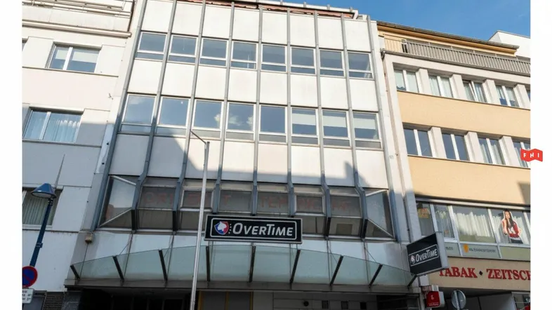 Fassade eines Geschäftsgebäudes mit großen Fenstern und Werbeschildern in einer städtischen Umgebung.