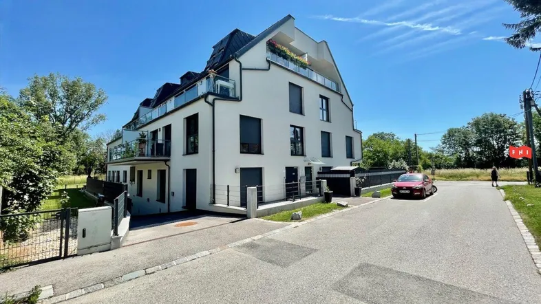 Modernes Mehrfamilienhaus mit weißer Fassade, Balkonen und Dachschrägen unter blauem Himmel.